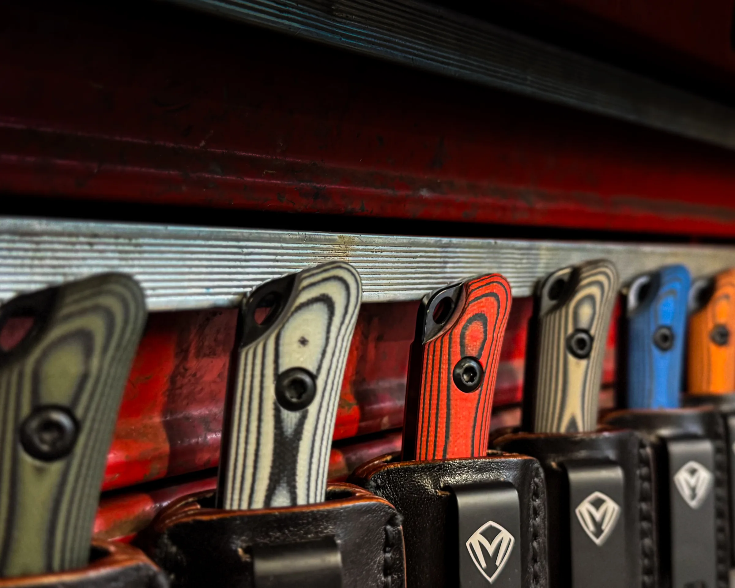 Taskmaster knives in multiple handle colors lined up in sheaths